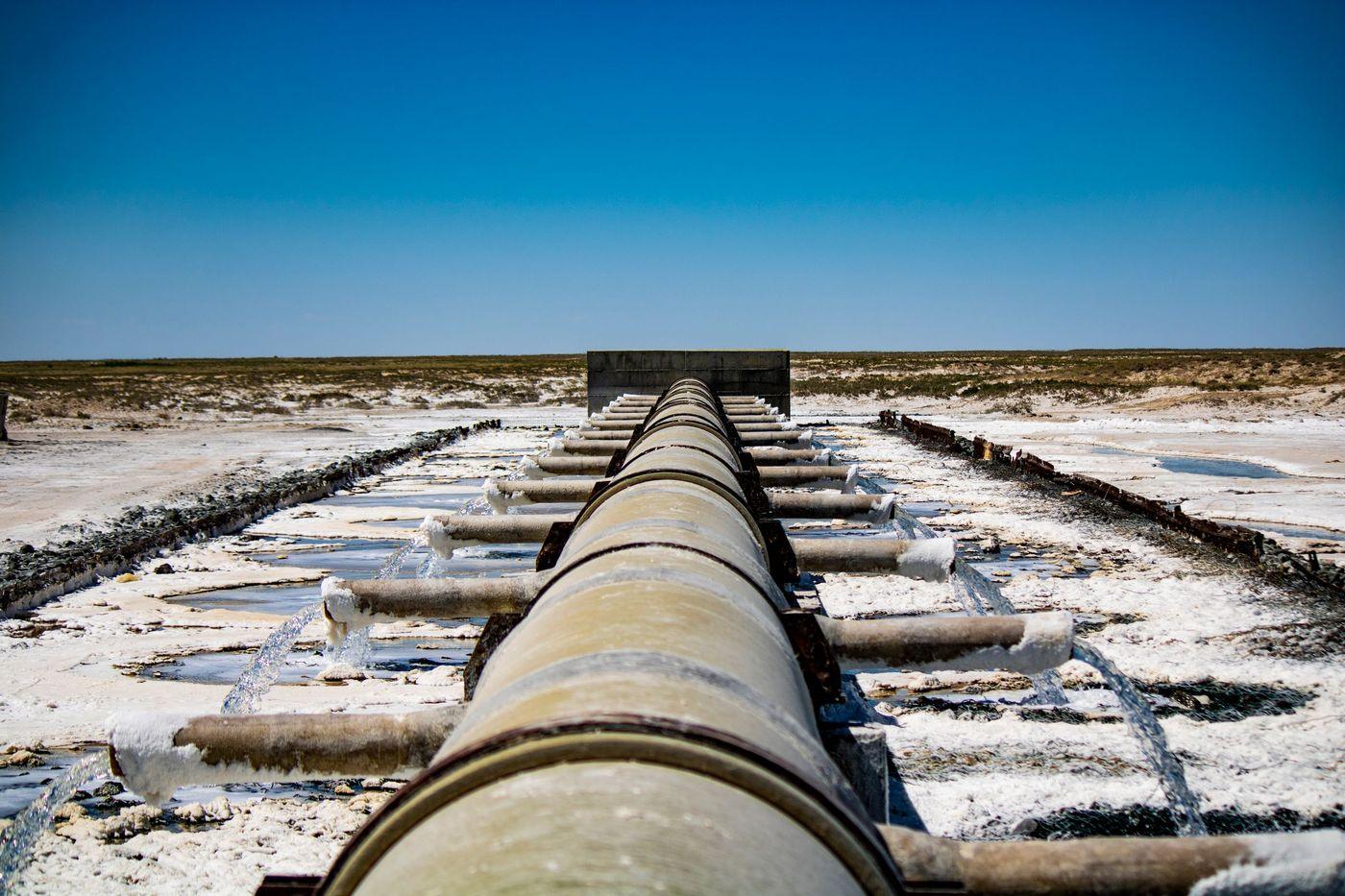 An industrial pipeline running water out across dry, open ground at a coastal treatment facility